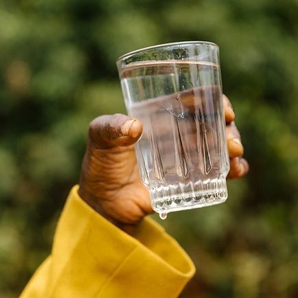 person with yellow shirt holding clear glass of water with one hand