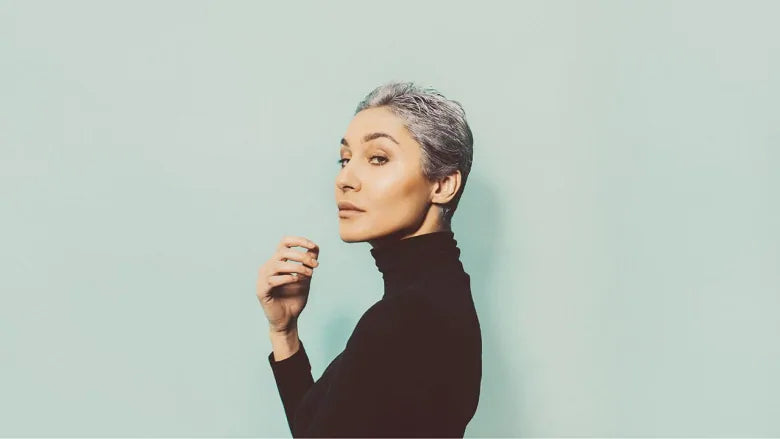 woman with grey short hair standing in front of a blue background