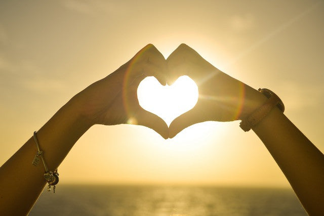 two hands coming together to create a heart with sunlight shining through