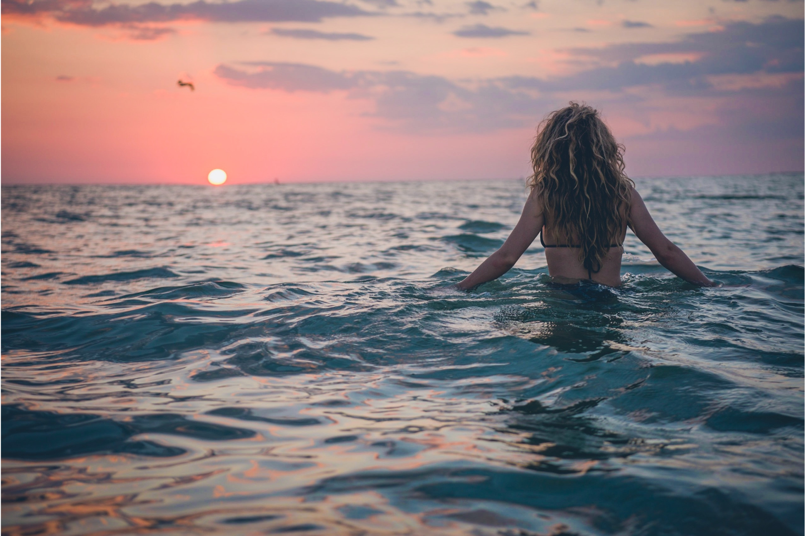 woman in the ocean facing the sunset