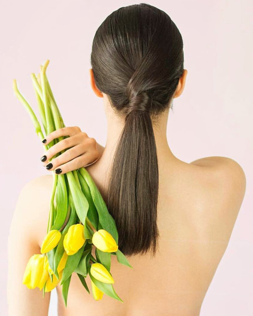 woman with shiny sleek brunette ponytail after using TO112 products holding yellow tulips over her shoulder