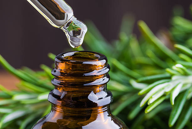 Rosemary oil being dropped into bottle with dropper fresh rosemary in background