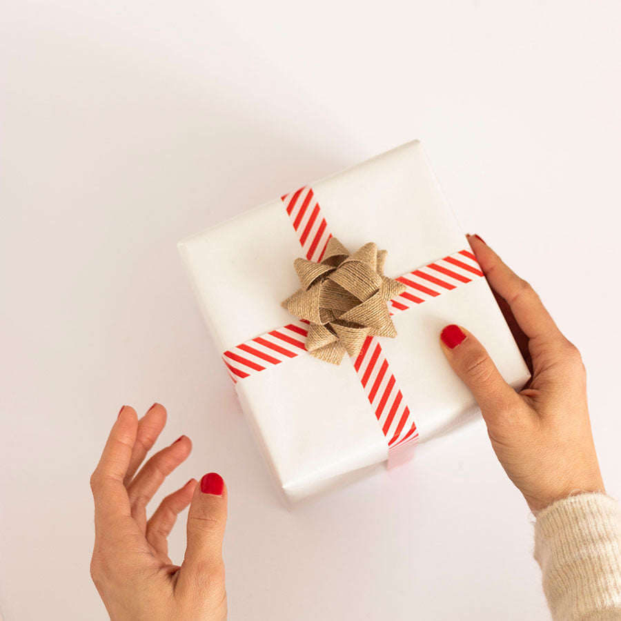 person with red nail polish receiving gift wrapped in white paper and red striped ribbon